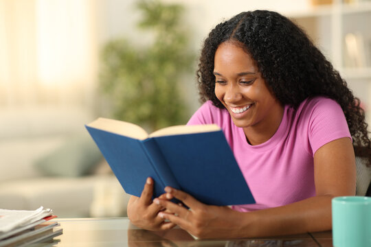Happy black woman reading a paper book at home