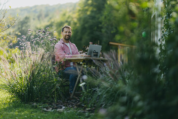 Man working in the garden, with laptop on legs. Businessman working remotely from outdoor homeoffice, thinking about new business or creative idea.