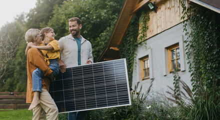Family walking in garden holding solar panel. Solar energy and sustainable lifestyle of young...