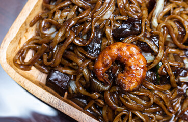 Close up of Jajangmyon serving on wooden plate. Chinese-style Korean noodle dish topped with a thick black sauce made of chunjang, diced pork, and vegetables.