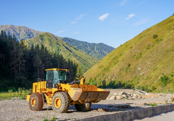 Tractor with a bucket on a gravel road in the mountains