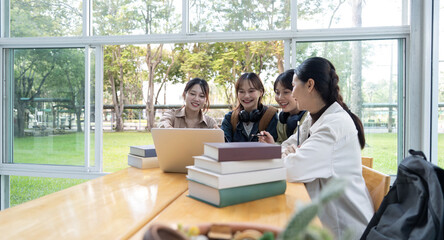 University students sitting together at table with book and laptop. Happy young people doing group study in college campus