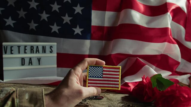 Soldier holding a USA patch with a flag and rose in the background 