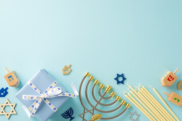 Jewish Tradition: Overhead view of menorah, Star of David symbols, gift box with bow, candles, and dreidel on a soft blue surface—ideal for your text or advertisement - obrazy, fototapety, plakaty