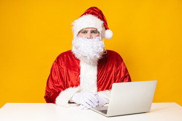 Santa Claus, at the table with a laptop, on a yellow background.