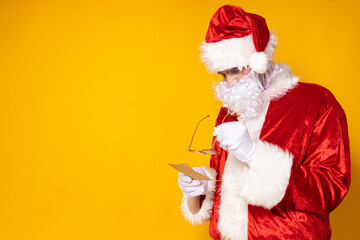 Obraz na płótnie Canvas Santa Claus with a phone on a yellow background.