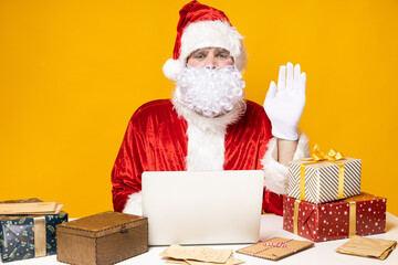 Santa Claus, at the table with a laptop, on a yellow background.