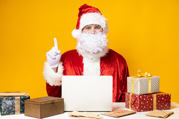 Santa Claus, at the table with a laptop, on a yellow background.