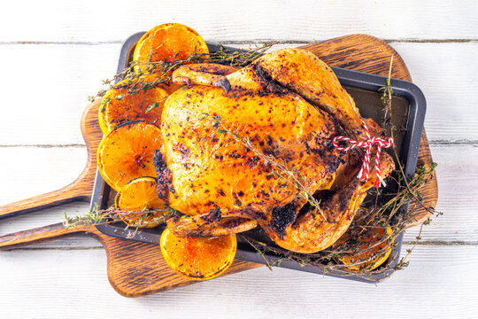 Christmas and Thanksgiving traditional baked chicken. Whole roasted chicken for holiday dinner, with oranges and thyme, on Christmas or Thanksgiving decorated table