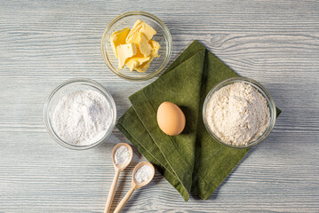 On a wooden table: baking ingredients, green napkin, wooden spoons, baking soda, dry yeast....