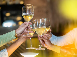 A close-up of friends raising their glasses in a toast, celebrating with chilled white wine. The...