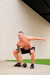 Strong man doing dumbbell squat snatch in a outdoor fitness gym. Cross fit, fitness and sport.