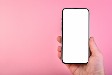 Hand holding smartphone with white screen on pink background with copy space.