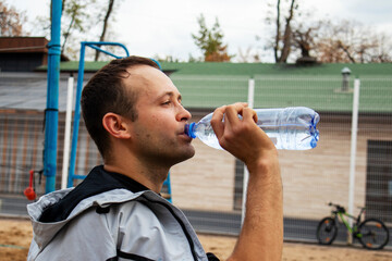 a guy drinks water from a bottle on the background of a street volleyball court