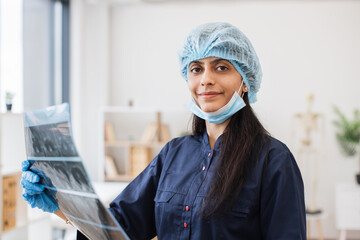 Portrait of hindu medical worker dressed in dark blue uniform and disposable cap holding result of...