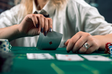attractive girl in shirt and hat covering face with hat holding poker cards in casino. poker - obrazy, fototapety, plakaty