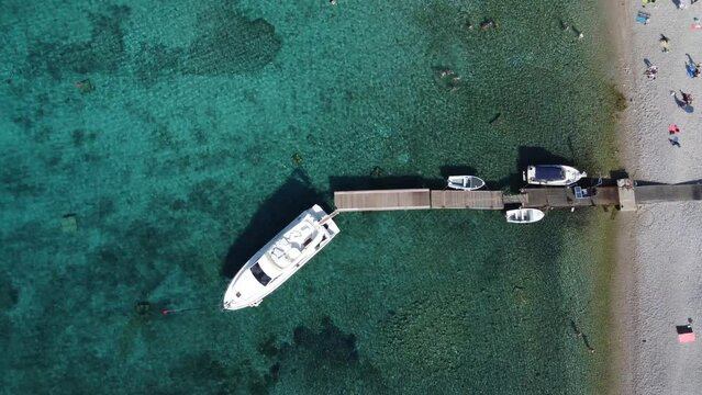 People swimming and relaxing on beach of Budikovac blue lagoon with yacht and dinghy boats at jetty. Aerial