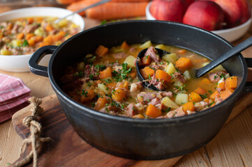 Stew with carrots, potatoes and smoked pork meat on wooden table in a pot