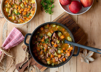 Carrot potato stew with smoked pork meat in a pot on wooden table