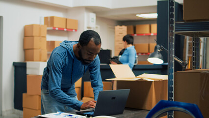 Male entrepreneur taking supplies from storage shelves to prepare merchandise order in storehouse. Young employee selling goods and working on business development, retail delivery.