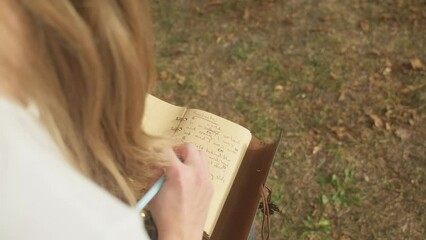 Over shoulder shot young blonde woman writes poetic lyrics in book