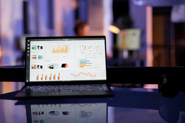 Laptop computer with marketing statistics standing on desk table in startup office, in background...