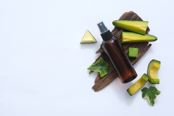 The right corner of the frame is decorated with an unlabeled brown hair spray bottle, surrounded by fresh avocados and green leaves. Blank space on the left for image design and more.