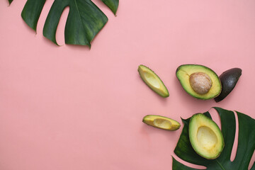 Fresh avocado with green leaves on pink background. Eating avocado helps nourish smooth and healthy skin from deep within, while also helping to scrub pores and exfoliate dead cells. Flat lay.