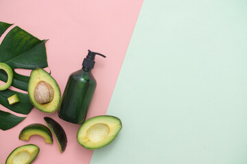 Avocado extract in cosmetic bottle, fresh avocado and green leaf on a pink background, pastel blue background for text and image design, top view, photography concept
