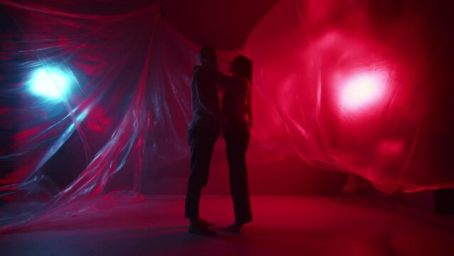 A young couple is kissing in the studio. Two lovers kisses indoors. Beautiful family hugs and flirting on neon light background. Sensual pair romantic foreplay