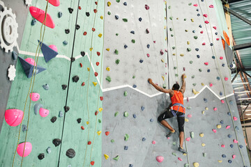 muscular young african american man climbing up bouldering wall gripping strongly on rocks © LIGHTFIELD STUDIOS