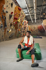 vertical shot of handsome african american man chilling with water bottle in hands and looking away