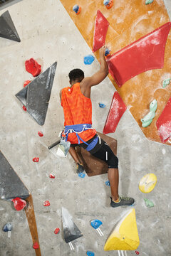 vertical shot of young african american man climbing up rock wall, back view, bouldering concept