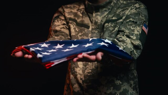 Soldier holding out triangle folded USA flag, army funeral, tribute symbol