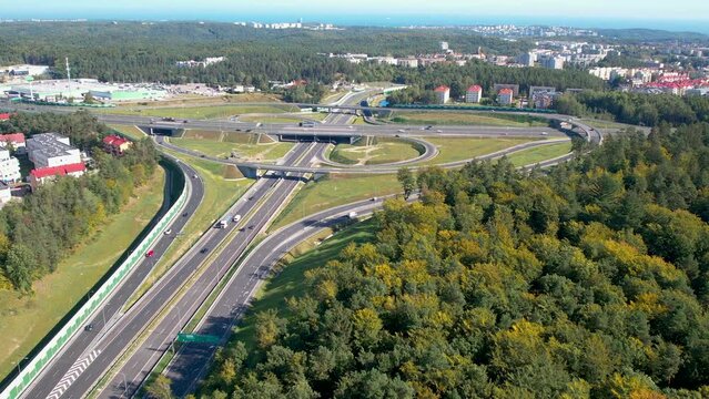 Aerial shot of a sprawling highway interchange surrounded by lush greenery and urban structures.