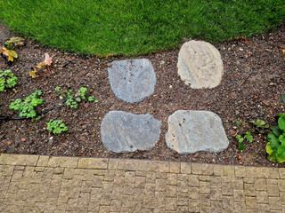 stepping stones lead to a small circular lawn in the middle of a flower bed. sitting on a bent...