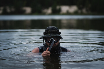 A military swimmer with a knife in his hand in the water at dusk.