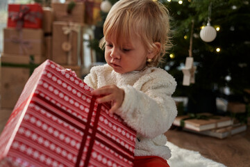 Cheerful caucasian toddler unpacking Christmas present