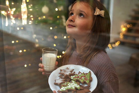 Little Girl Looking Through The Window And Waiting For Santa Claus