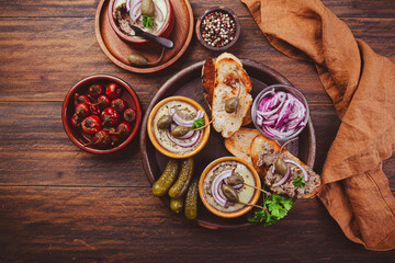 Fresh homemade chicken liver pate in ceramic bowls and appetizers on rustic background