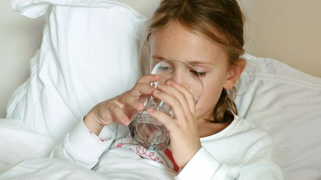 Health stay hydrated concept. Thirsty Child Drinking Water at home in pajamas. Kid drink fresh pure water glass cup siting on bed. Take care body. Morning routing. Hydration tips for children