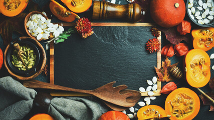 Autumn card. Kitchen board, pumpkin, autumn dry leaves and autumn flowers. On a dark stone background. Thanksgiving day.