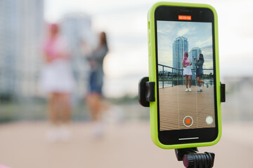 Two cheery girls recording videos with smartphone for their social media vlog on city waterfront