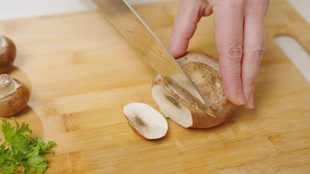 Woman slicing royal champignon mushroom with knife on cutting board.