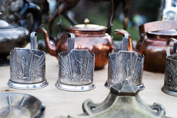 Vintage copper and metal antiques, tableware, jugs, glass holders on a counter at a street flea...