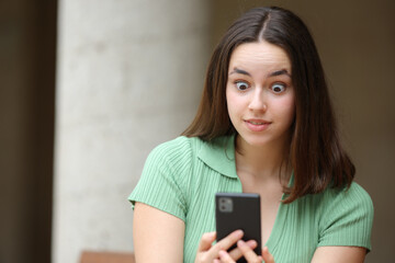 Shocked woman checking phone news in the street