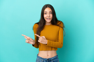 Young French woman isolated on blue background frightened and pointing to the side