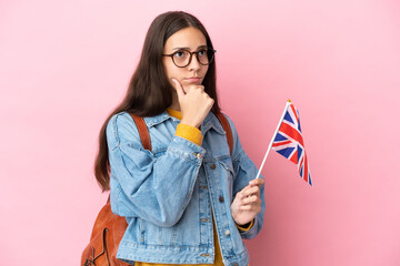 Young French girl holding an United Kingdom flag isolated on pink background having doubts