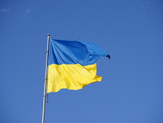 Flag of Ukraine in blue and yellow colors flutters in the air against the background of the blue sky. Slow motion