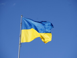 Flag of Ukraine in blue and yellow colors flutters in the air against the background of the blue sky. Slow motion